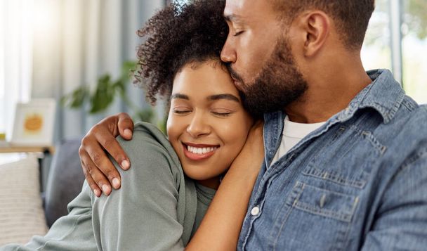 Young happy mixed race boyfriend kissing his girlfriend on the forehead while relaxing at home. Cozy hispanic husband and wife smiling while hugging in the lounge at home. - Valokuva, kuva