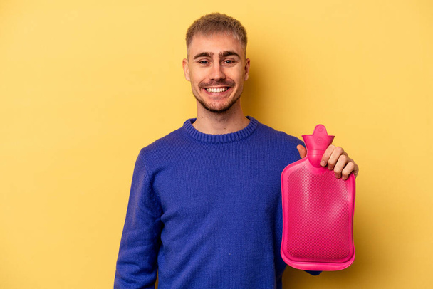 Young caucasian man holding a water bag isolated on yellow background happy, smiling and cheerful. - Fotografie, Obrázek