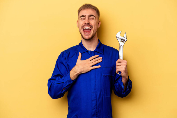 Young electrician caucasian man isolated on yellow background laughs out loudly keeping hand on chest. - Фото, зображення