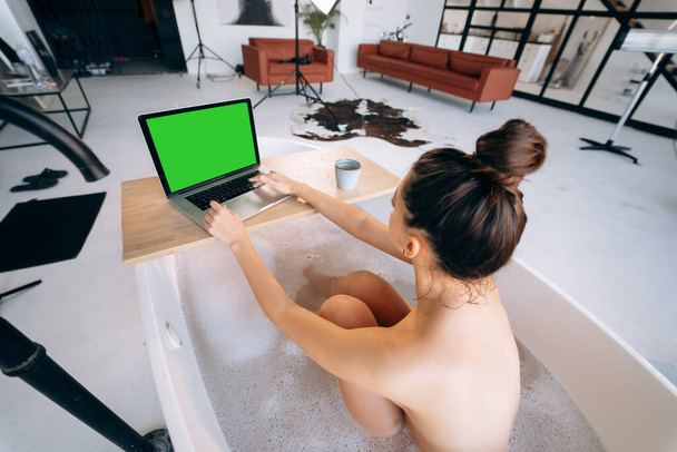 jonge vrouw werken op laptop terwijl het nemen van een bad thuis - Foto, afbeelding
