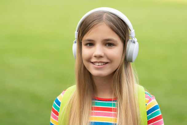 Happy teen girl listening to music in headphones outdoors, school. - 写真・画像