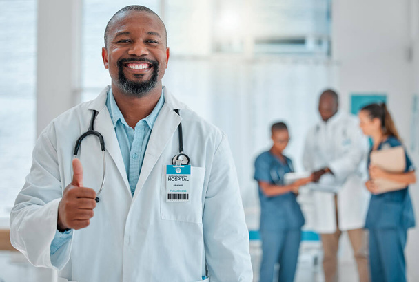 Mature african american male doctor showing a thumbs up while working at a hospital with colleagues. Expert medical professional smiling while making a hand gesture in support at work at a clinic. - Foto, afbeelding