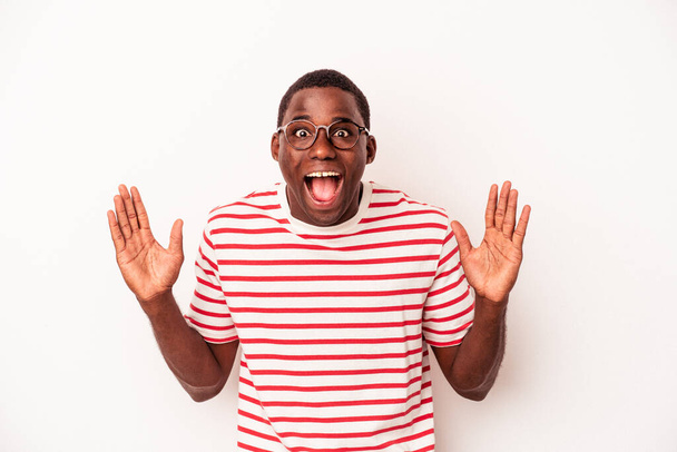 Νεαρός Αφροαμερικάνος, απομονωμένος σε λευκό φόντο, δέχεται μια ευχάριστη έκπληξη, ενθουσιασμένος και σηκώνει τα χέρια.. - Φωτογραφία, εικόνα