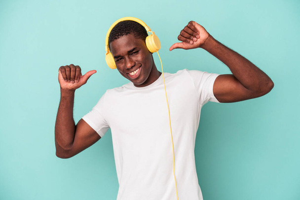 Young African American man listening to music isolated on blue background feels proud and self confident, example to follow. - Photo, Image