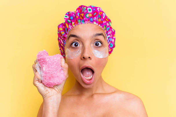 Young mixed race woman with shower cap holding a sponge isolated on yellow background - Photo, Image