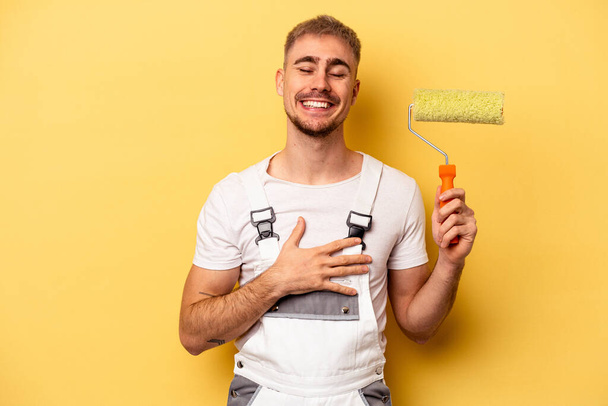 Young painter man isolated on yellow background laughing and having fun. - Fotó, kép