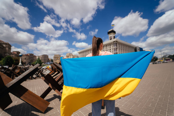 A young woman carries the flag of Ukraine fluttering behind her in the street - Fotoğraf, Görsel