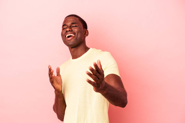 joven afroamericano hombre aislado en rosa fondo se siente seguro de dar un abrazo a la cámara. - Foto, Imagen