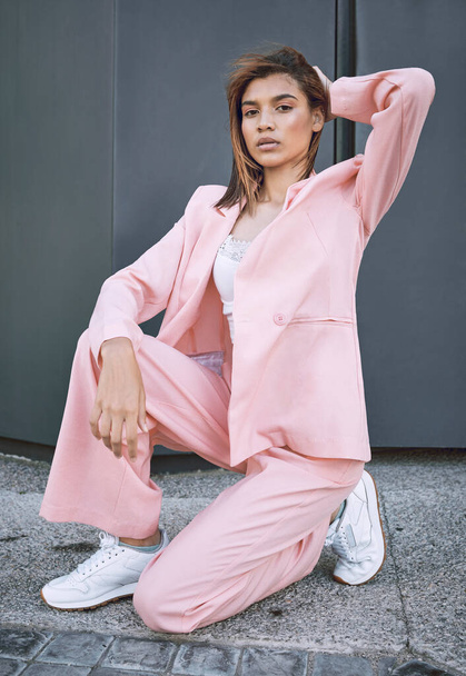 Portrait of a young trendy and confident mixed race woman looking stylish while posing and spending time in the city. Fashionable hispanic female model wearing pink clothes and kneeling on the - Fotografie, Obrázek