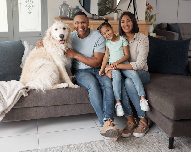 Portrait of a happy mixed race family of three relaxing on the sofa with their dog. Loving black family being affectionate with a foster animal. Young couple bonding with their daughter and rescued - Φωτογραφία, εικόνα
