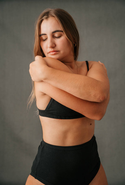 Portrait of blond Caucasian female eyes close and hugging herself posing in the studio. High quality photo - Valokuva, kuva