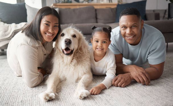 Portrait of a happy mixed race family of three relaxing on the lounge floor with their dog. Loving black family being affectionate with a foster animal. Young couple bonding with their daughter and - Foto, afbeelding