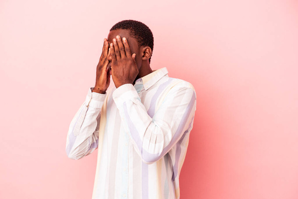 Νεαρός Αφροαμερικάνος, απομονωμένος σε ροζ φόντο, φοβάται να καλύψει τα μάτια με τα χέρια.. - Φωτογραφία, εικόνα