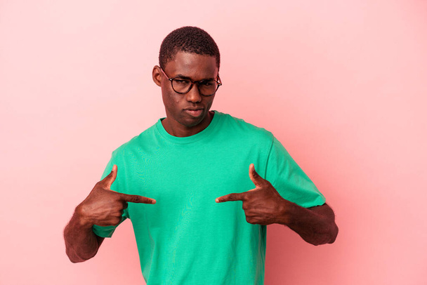 Mladý africký Američan izolovaný na růžovém pozadí osoba ukazuje ručně na košili kopírovací prostor, hrdý a sebejistý - Fotografie, Obrázek