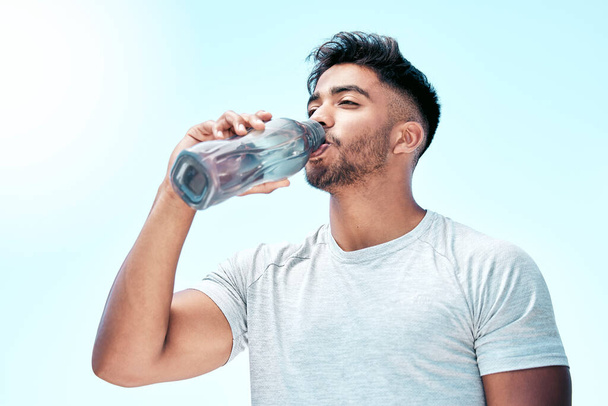 Fit young mixed race man drinking water from a bottle while exercising outdoors. Handsome hispanic male taking a sip of water during a break from his workout outside. Cardio and endurance training. - Foto, afbeelding