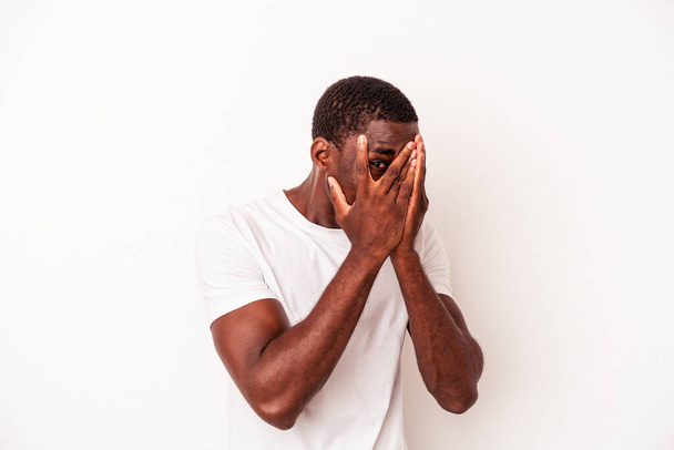 Νεαρός Αφροαμερικάνος απομονωμένος σε λευκό φόντο αναβοσβήνει μέσα από τα δάχτυλα φοβισμένος και νευρικός. - Φωτογραφία, εικόνα