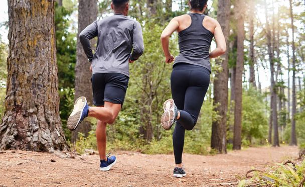 Fit male and female athletes running in nature. Young sportspeople couple out for a workout in the forest. Keeping fit and staying healthy together. - Foto, imagen
