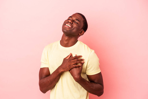 Νεαρός Αφροαμερικάνος απομονωμένος σε ροζ φόντο γελώντας κρατώντας τα χέρια στην καρδιά, την έννοια της ευτυχίας. - Φωτογραφία, εικόνα