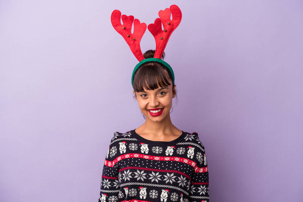 Jonge gemengde ras vrouw met rendieren hoed vieren Kerstmis geïsoleerd op paarse achtergrond gelukkig, glimlachend en vrolijk. - Foto, afbeelding