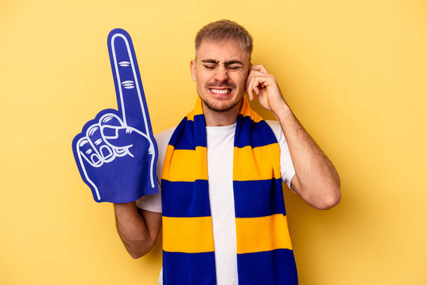 Young sports fan caucasian man isolated on yellow background covering ears with hands. - Foto, immagini