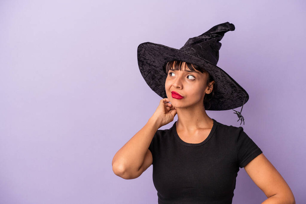 Young mixed race woman disguised as a witch isolated on purple background  touching back of head, thinking and making a choice. - Фото, зображення