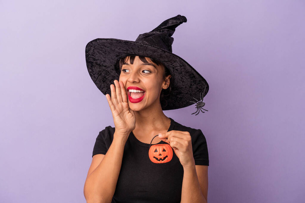 Young mixed race woman disguised as a witch isolated on purple background  shouting and holding palm near opened mouth. - Photo, Image