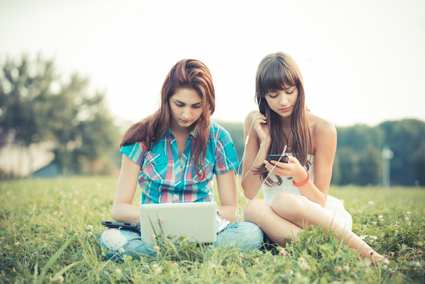 Sisters using tablet and smartphone in the park - Photo, Image