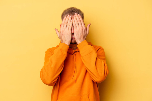 Young caucasian man isolated on yellow background having fun covering half of face with palm. - Fotoğraf, Görsel