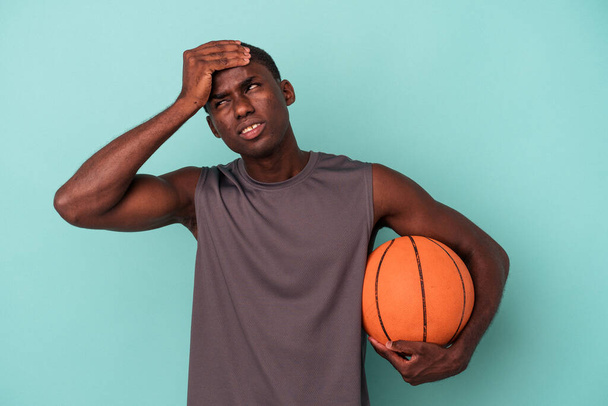 Young African American man playing basketball isolated on blue background being shocked, she has remembered important meeting. - Photo, Image