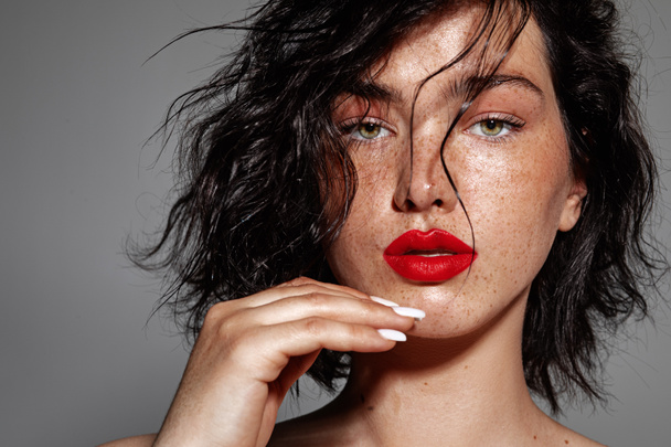 beauty young woman face with a lot of freckles and red lips, hand near face, close up - Fotó, kép