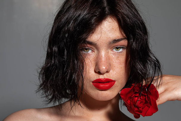 beauté jeune femme visage avec beaucoup de taches de rousseur et lèvres rouges, rose rouge près du visage, gros plan - Photo, image