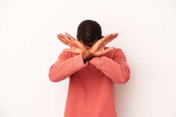 Молодой африканский американец, изолированный на белом фоне, держащий две руки скрещенными, концепция отрицания. - Фото, изображение