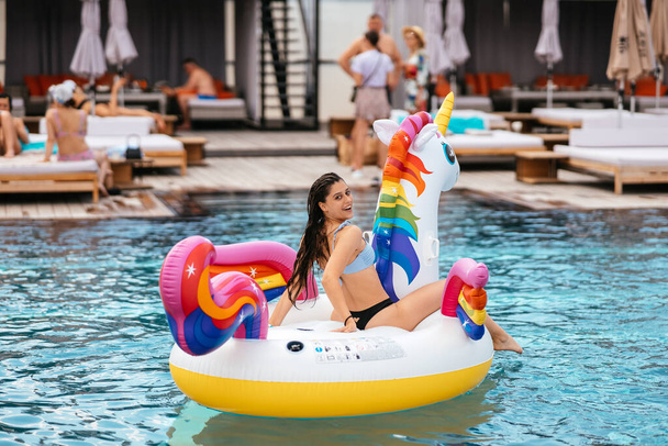 Woman in bikini in inflatable unicorn toy mattress float in pool. Girl relaxing sunbathing enjoying travel holidays at resort pool - Photo, image