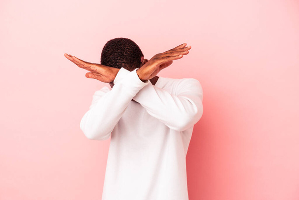 Jonge Afro-Amerikaanse man geïsoleerd op roze achtergrond houden van twee armen gekruist, ontkenning concept. - Foto, afbeelding