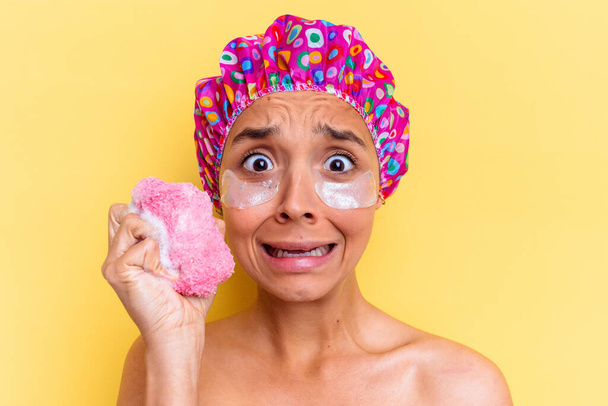 Joven mujer de raza mixta tomando un baño sosteniendo una esponja con un parche debajo de los ojos - Foto, imagen
