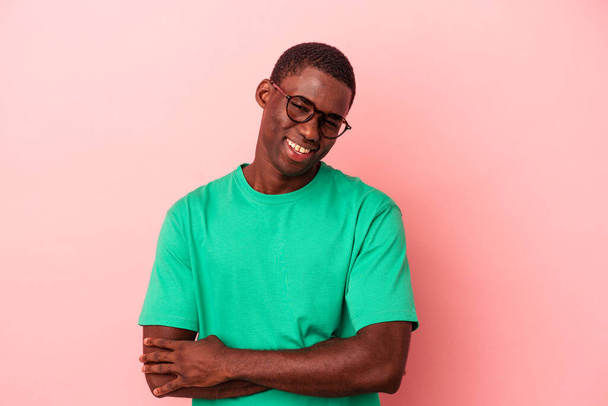 Giovane uomo afroamericano isolato su sfondo rosa che si sente fiducioso, incrociando le braccia con determinazione. - Foto, immagini