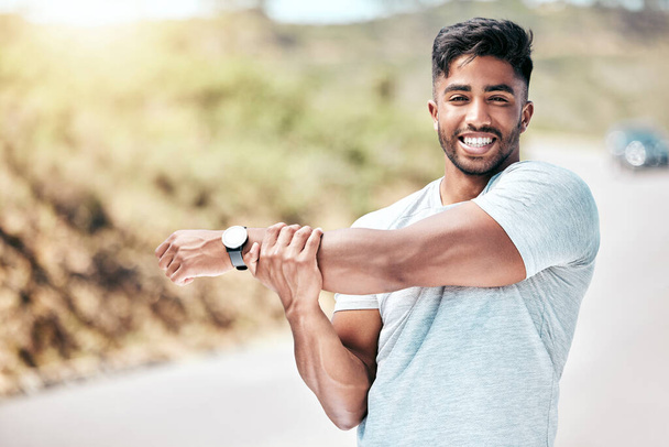 Fit young mixed race man stretching before his exercise outdoors. Handsome hispanic male warming up and getting ready in preparation for a run or jog outside in nature. Endurance and cardio training. - 写真・画像