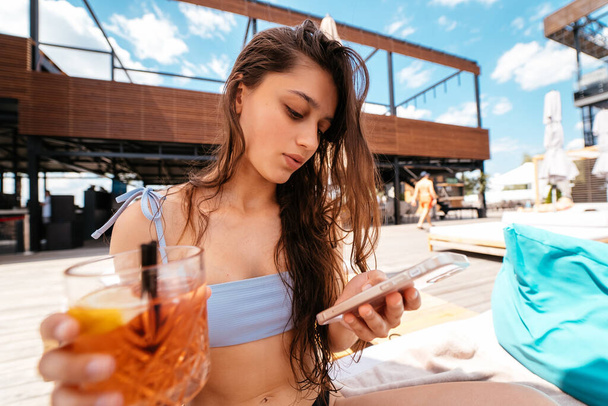 Attractive young woman with cellphone chatting online in swimming pool outside, panorama - Фото, изображение