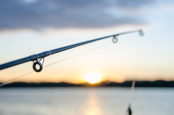 fishing rod with lure at sunset over a lake - Photo, Image