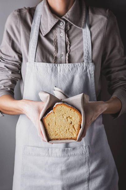 A girl in an apron and a shirt holding a white biscuit with powdered sugar in her hands with a towel - Fotoğraf, Görsel