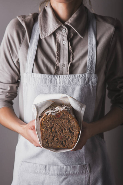 A girl in an apron and a shirt holding a chocolate sponge cake with powdered sugar and candied fruits in her hands with a towel - Foto, Bild