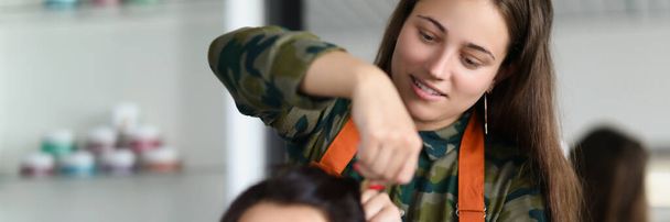 Portrait of smiling hairdresser creating fancy hairstyle for female client. Prepare woman for important event in beauty salon. Wellness, barbershop concept - Foto, imagen