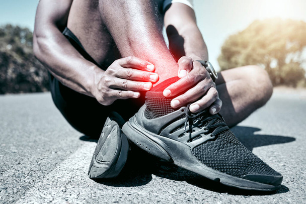 Closeup fit mixed race man holding his ankle in pain while exercising outdoors. Unrecognizable male athlete suffering with a joint injury highlighted by glowing cgi. You can get hurt during a workout. - Fotografie, Obrázek