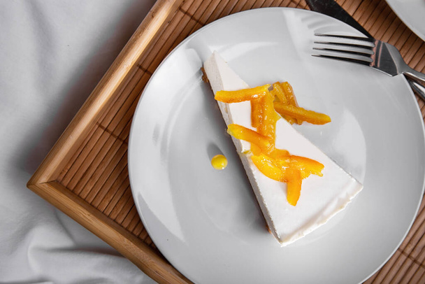 Cheesecake with apricot pieces in a plate with cutlery on a wooden board and white table - Foto, Imagem
