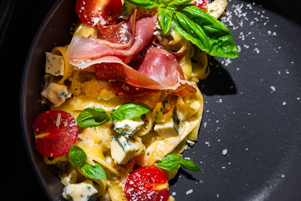 Spaghetti with prosciutto, tomatoes, basil, blue cheese and parmesan in a plate on a green table - Foto, afbeelding
