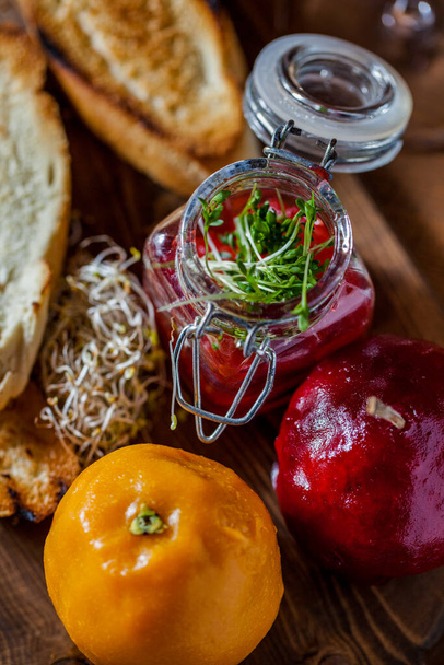 Wild boar liver pate in sweet glaze in the form of orange and Sicilian orange, microgreen onion sprouts, French baguette toast, cherry sauce in a glass jar with a metal clip and a glass lid. Food stands on a wooden board. The board lies on a wooden b - Photo, Image