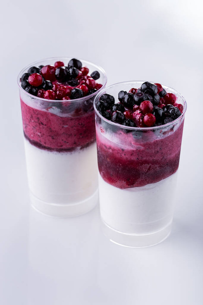 Vanilla ice cream with blueberries and lingonberries in two glasses on a light background. Vertical orientation - Zdjęcie, obraz