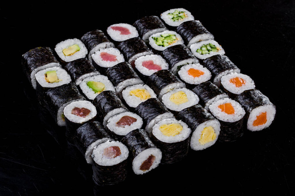 Суши-тунец, омлет, авокадо, лосось, огурец на черном фоне - Фото, изображение