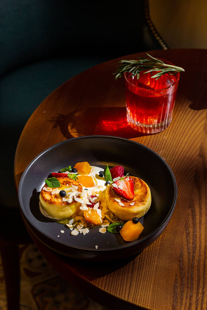 Cheese pancakes with mango, strawberry, raspberry, almond slices, mint and sauce in a plate on the table with a glass of juice and rosemary - Foto, immagini