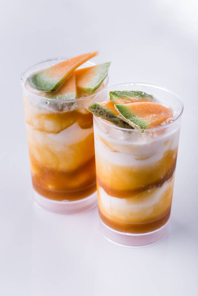 Ванильное мороженое в двух стаканах с джемом из дыни и кусочками дыни на светлом фоне. Вертикальная ориентация - Фото, изображение